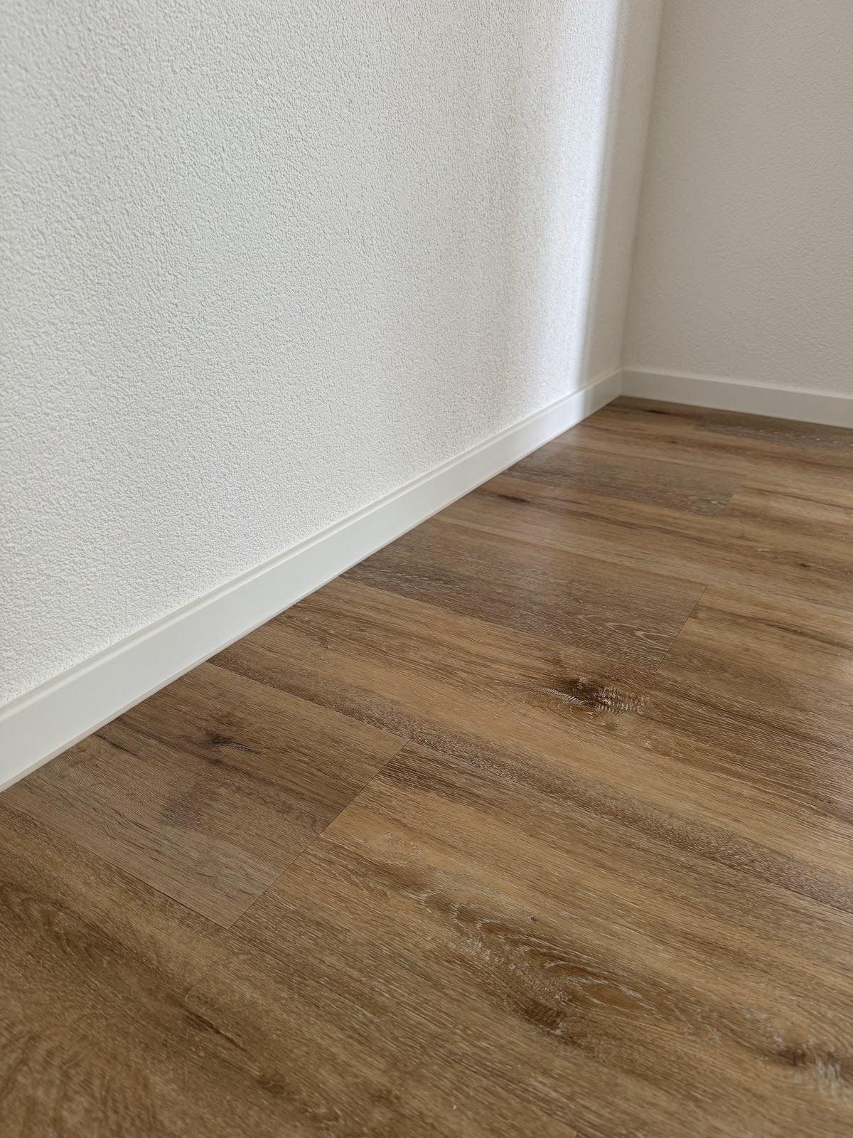 Detailaufnahme eines Vinylbodens in Holzoptik an der Sockelleiste